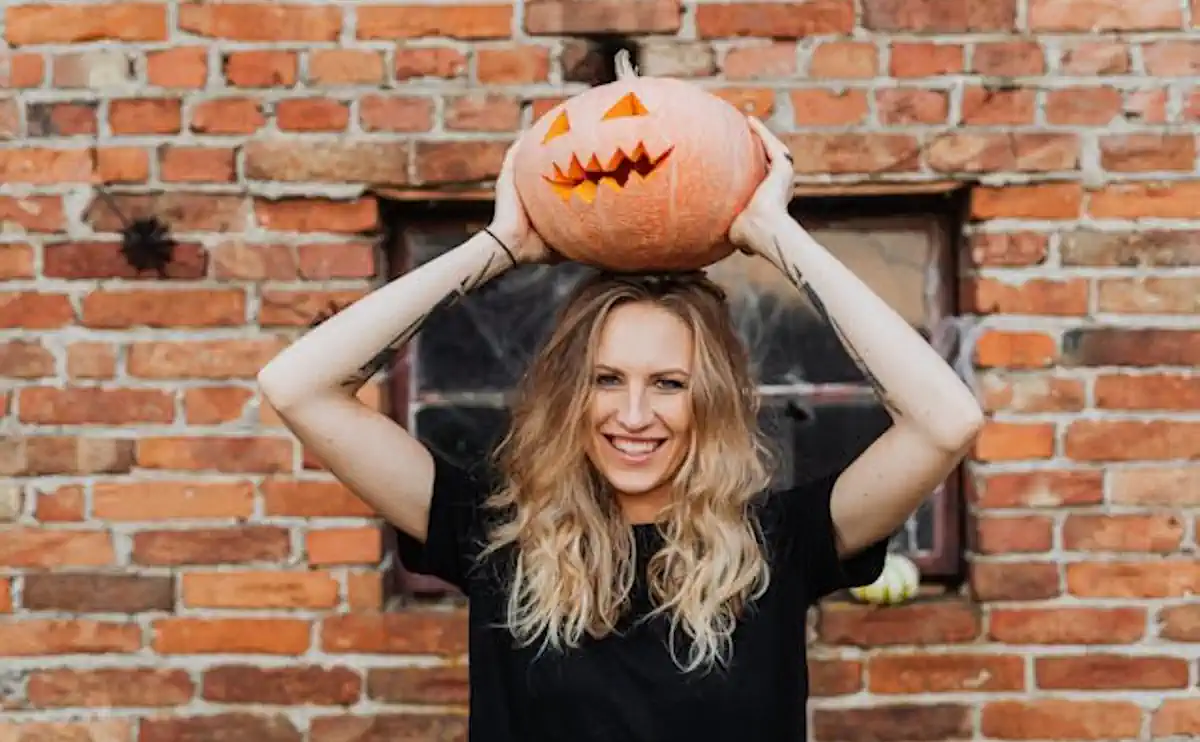 Woman wearing a pumpkin on her head, celebrating autumn ambiance with Lux Candles & Melts.